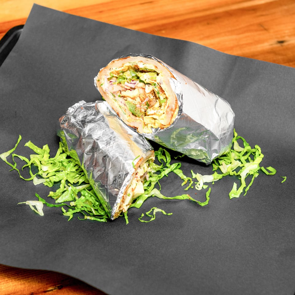 Foil-wrapped burrito cut open to reveal grilled chicken, lettuce, vegetables, and sauce on a black serving tray.