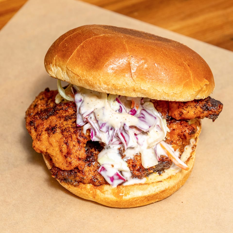 Grilled chicken sandwich on a toasted bun with creamy red cabbage slaw, served on parchment paper.